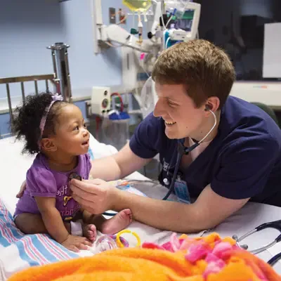 Male nursing 学生 using a stethoscope to care for a toddler child.