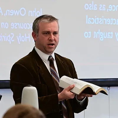 Bible professor holding an open Bible and teaching students